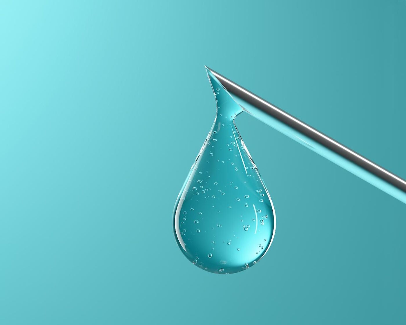 Transparenter Impfstoff-Tropfen an einer Pipette vor türkisfarbenem Hintergrund.